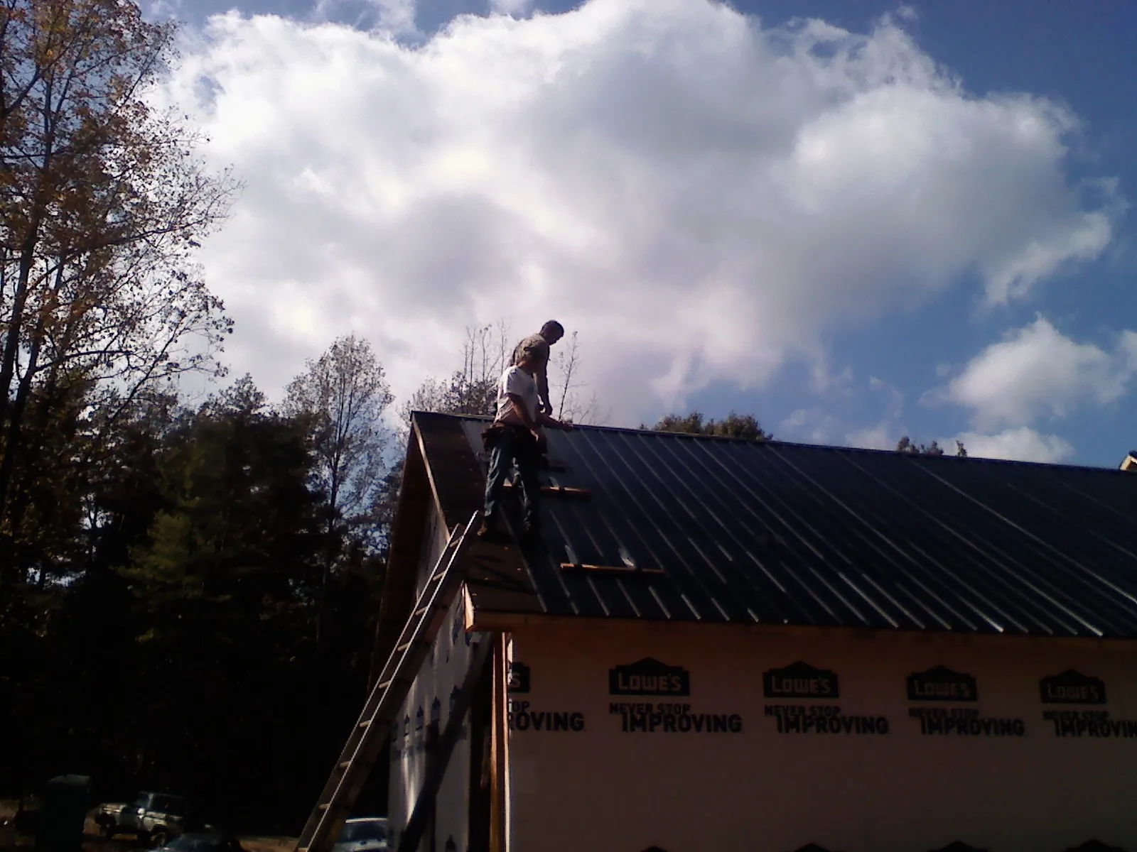 Roofer fastening dark metal panels high against a cloudy sky, from a Roof Inspection job in Township Of Washington