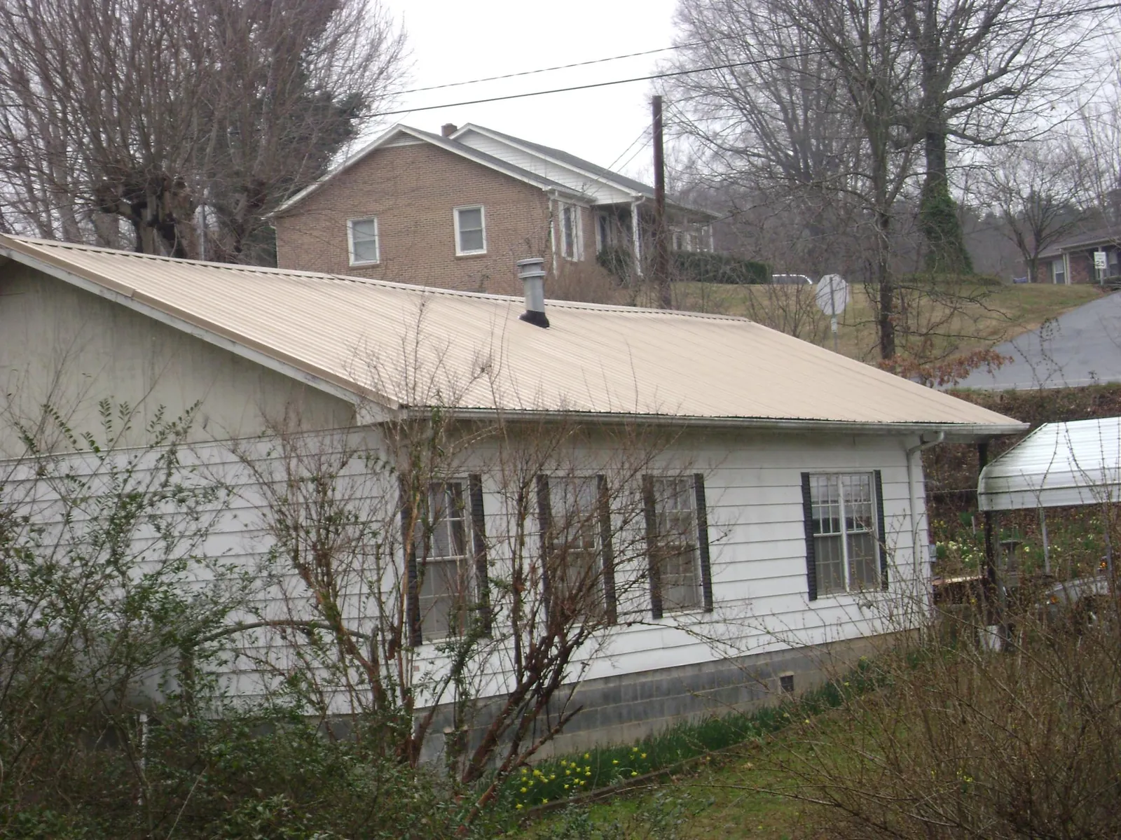 Tan metal roof on a white sided house set into a hillside — Commercial Roofing by Roofing Brothers in Township Of Washington